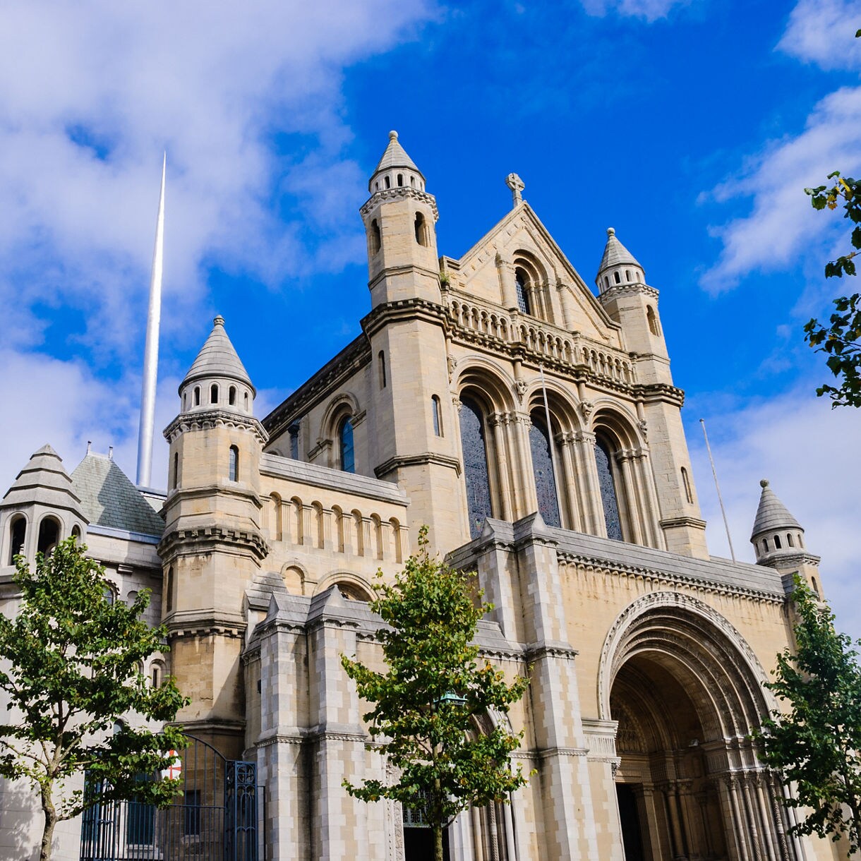 Belfast City Hall with green-domed towers and ornate facade, featuring the Queen Victoria Memorial statue in the front garden.