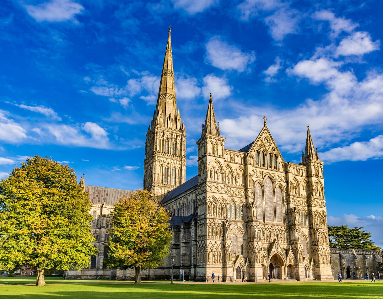 Gothic architecture of Salisbury Cathedral in Portland, with its soaring spire and ornate façade, surrounded by green lawns and autumn-colored trees under a clear sky