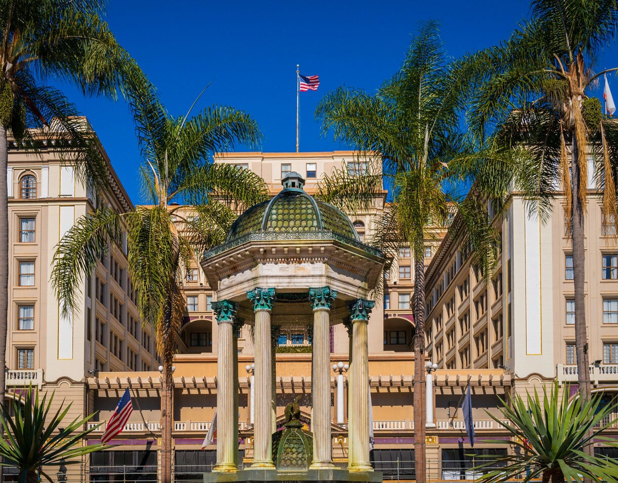 Ornate domed fountain surrounded by tall palm trees with the historic Horton Plaza buildings in downtown San Diego behind it.