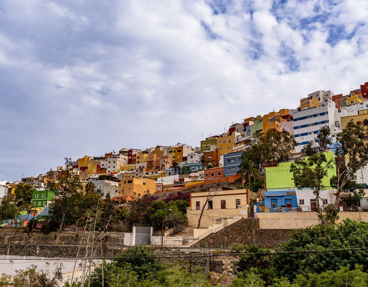 Colorful hillside houses of San Juan, Tenerife, with stacked buildings painted in bright shades of yellow, blue and red beneath a partly cloudy sky.
