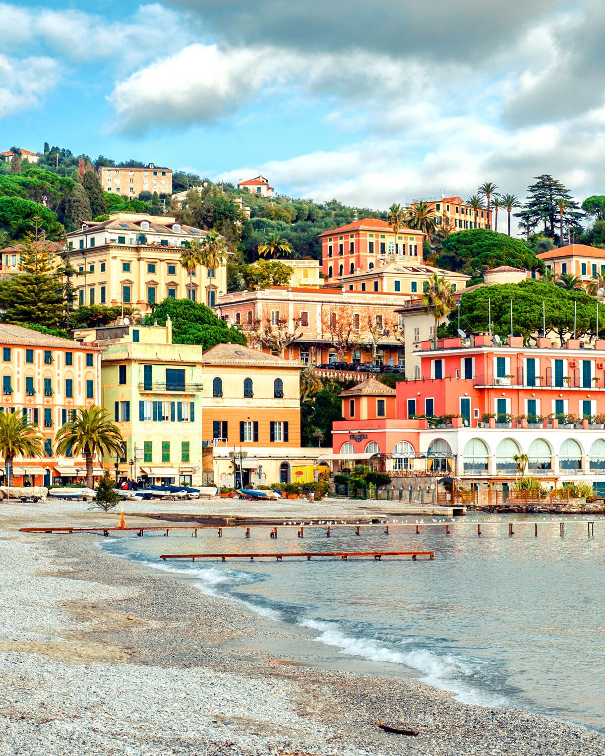 Colorful seaside buildings and palm trees along the waterfront of Santa Margherita Ligure, Italy, backed by lush green hills.