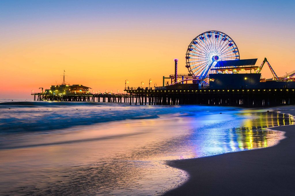 The Santa Monica Pier illuminated at dusk, with the Ferris wheel glowing against a vibrant orange and blue sky.