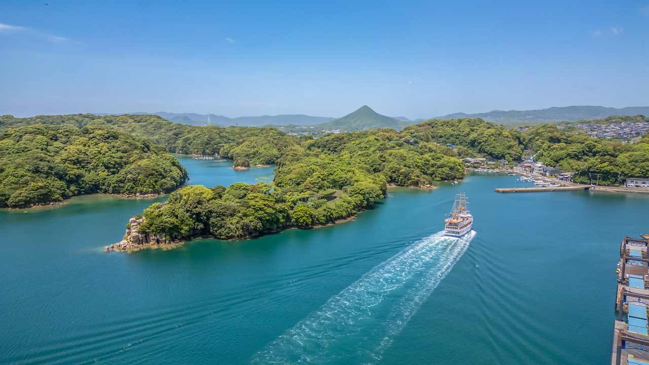 Sightseeing boat leaving port, sailing through lush green islands and calm blue waters near Sasebo, Japan.