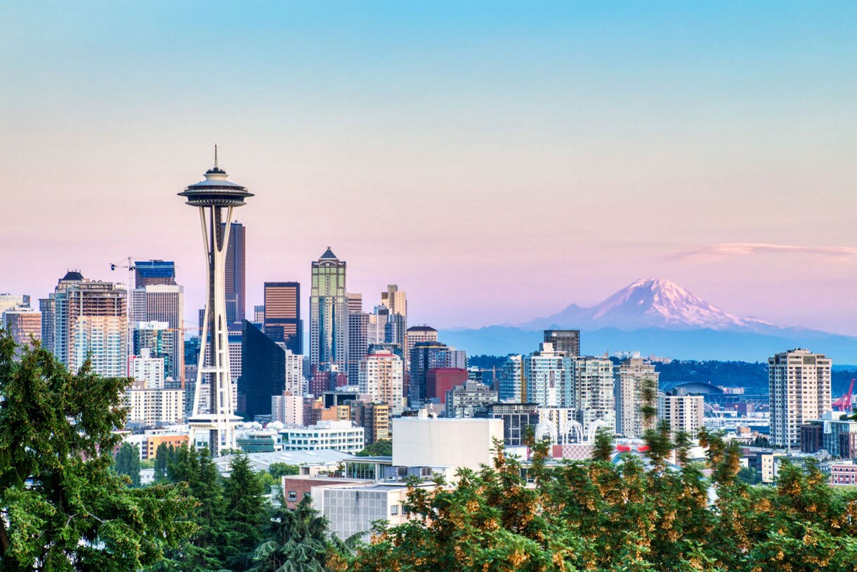 Seattle skyline at dawn with Mount Rainier visible in the background, framed by trees.