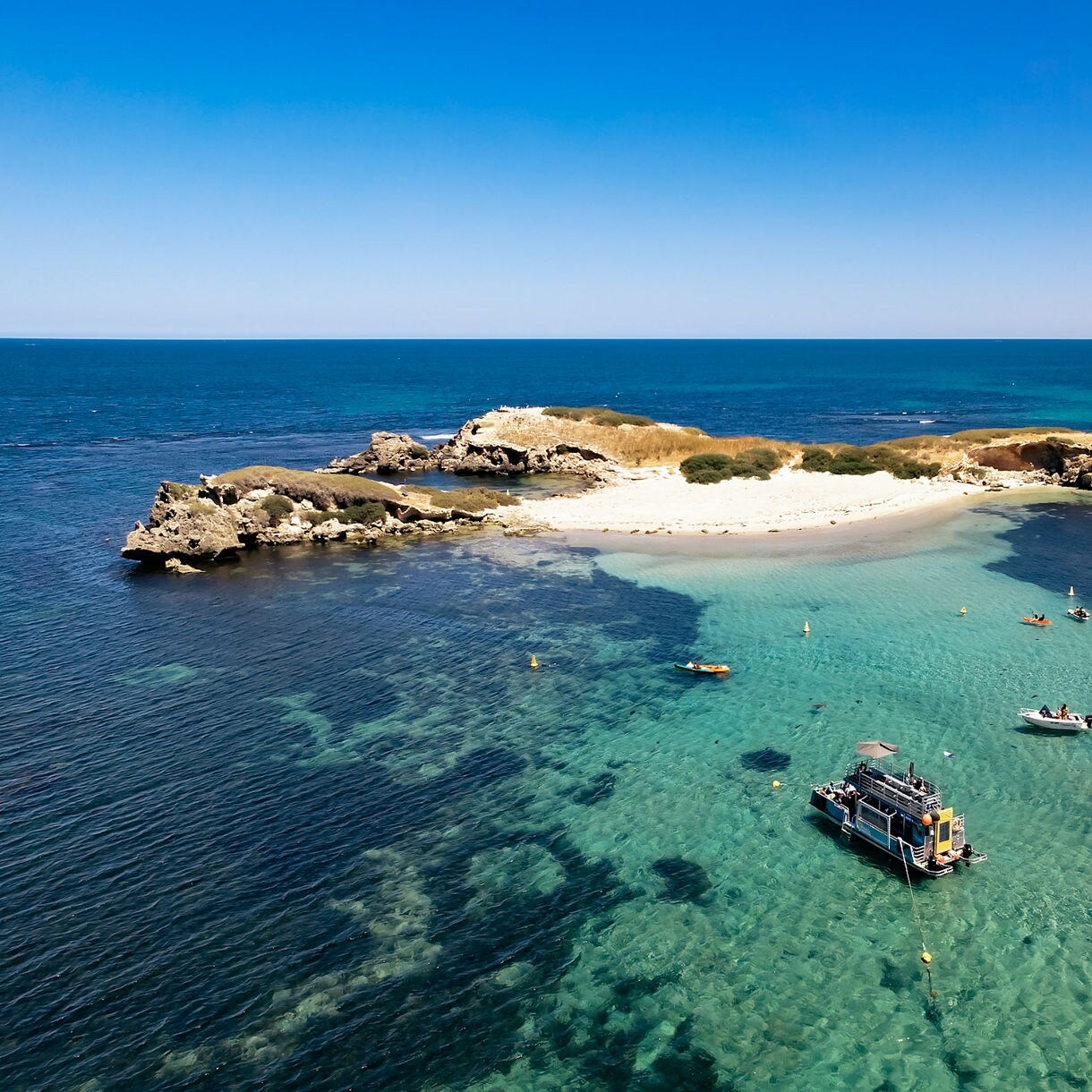 Aerial view of sandy island surrounded by turquoise water with boats and kayaks floating nearby in Shoalwater Islands Marine Park.
