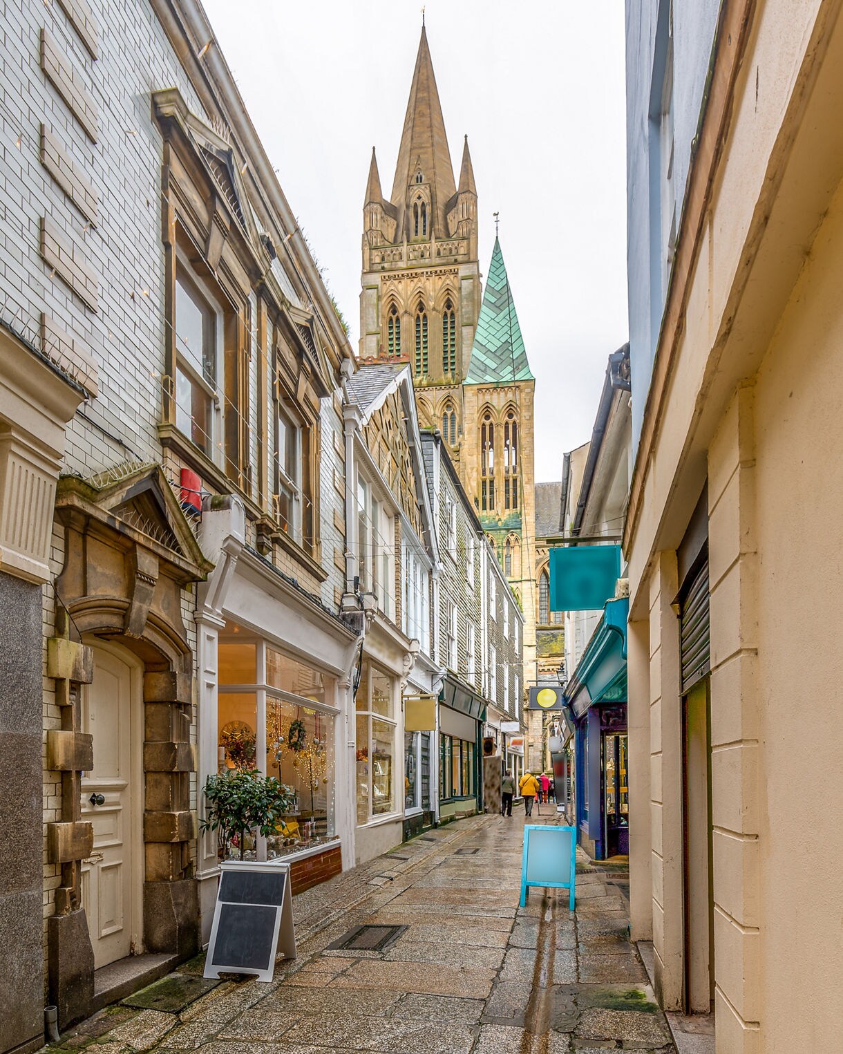 Narrow cobbled street in Truro lined with boutique shops, with Truro Cathedral’s tall spires rising in the background.