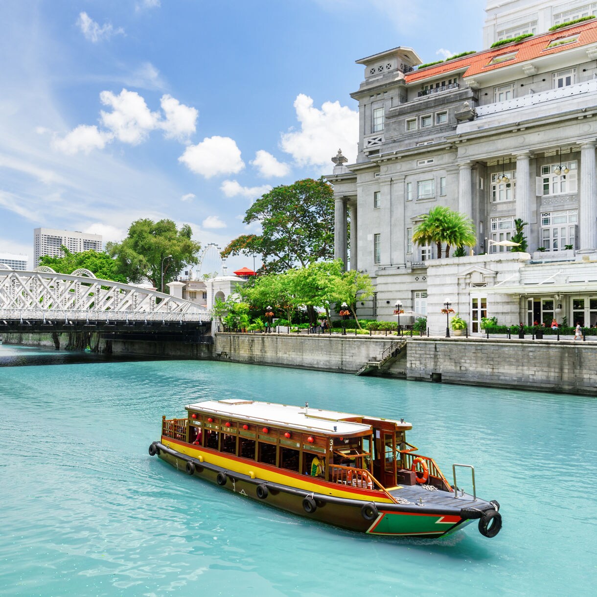 Wooden bumboats cruising the turquoise waters of the Singapore River beside colonial architecture and a steel bridge.