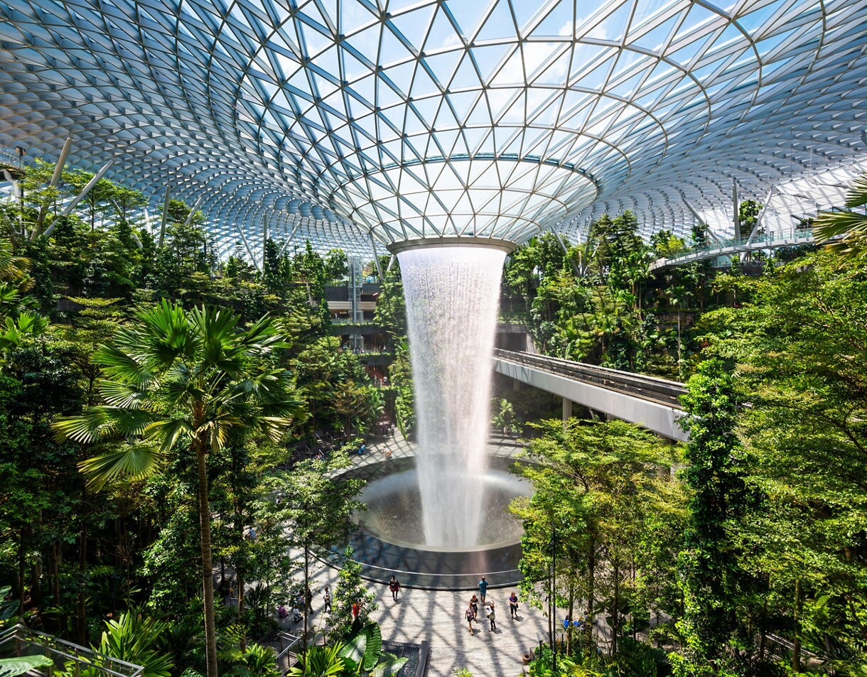 Indoor waterfall at Jewel Changi Airport in Singapore surrounded by tropical greenery beneath a vast glass dome.