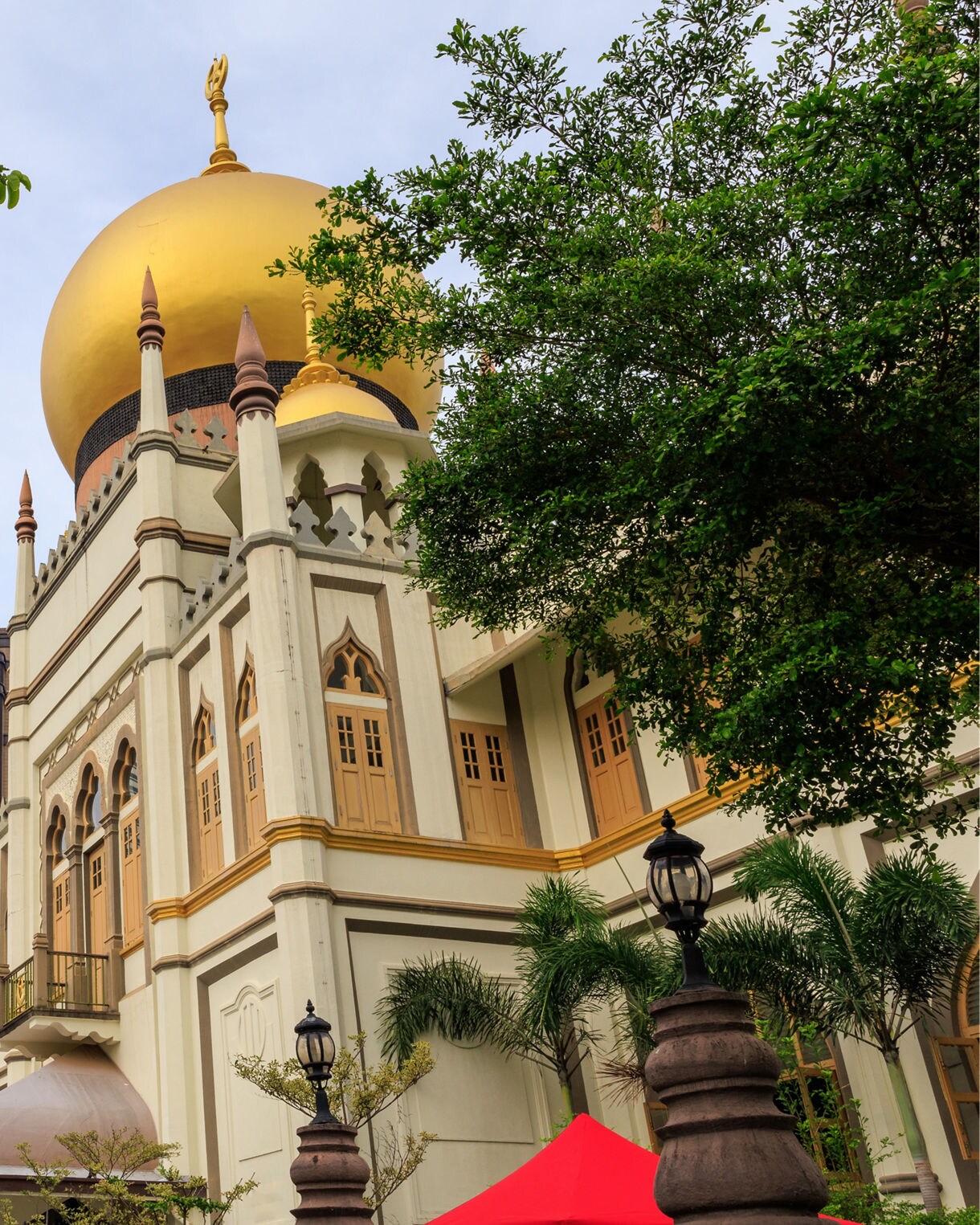 Sultan Mosque in Singapore’s Kampong Glam district with its striking golden dome framed by trees and nearby skyscrapers.