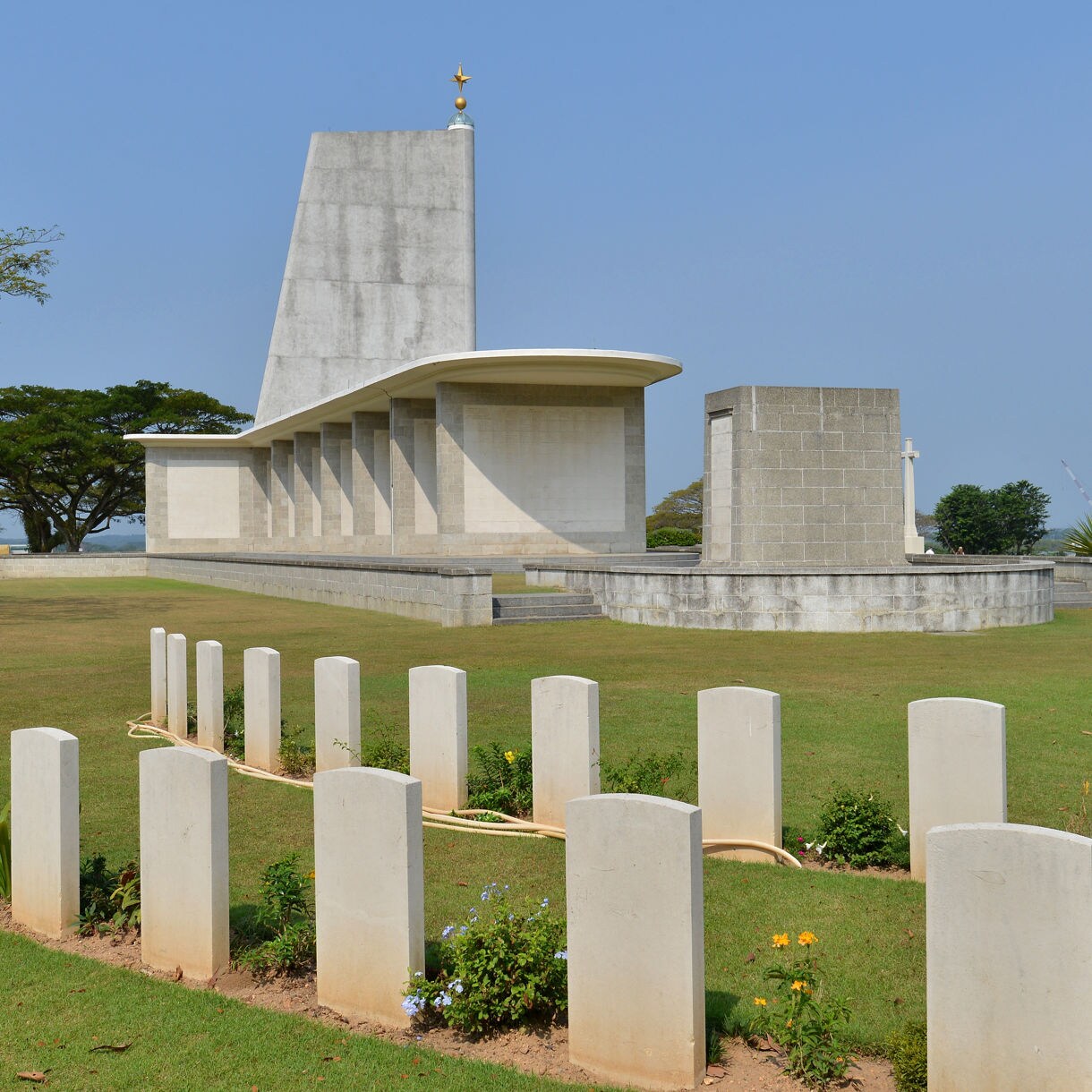 White gravestones leading to the Kranji War Memorial in Singapore, featuring a tall, modernist monument surrounded by manicured lawns.