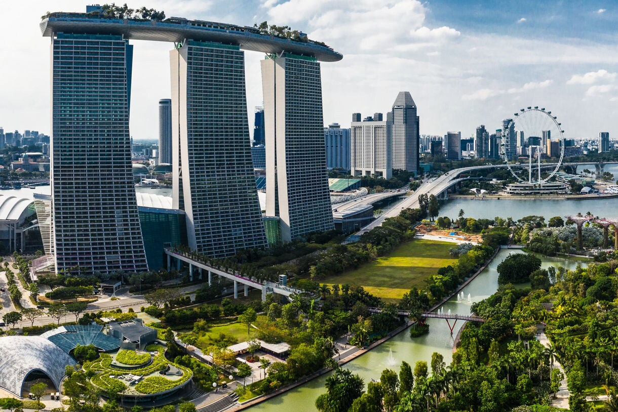 Aerial view of Singapore featuring Marina Bay Sands towers, Gardens by the Bay’s Supertree Grove, the Singapore Flyer, and modern high-rises along the waterfront.