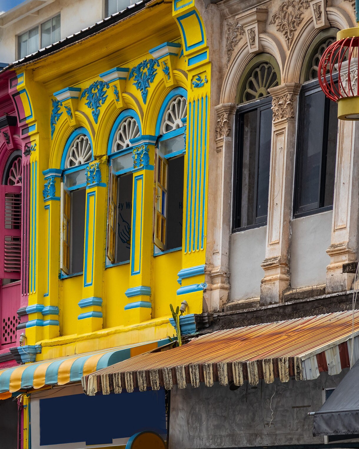 Row of brightly painted Sino-Portuguese shophouses in Phuket Old Town with ornate windows and colorful awnings.