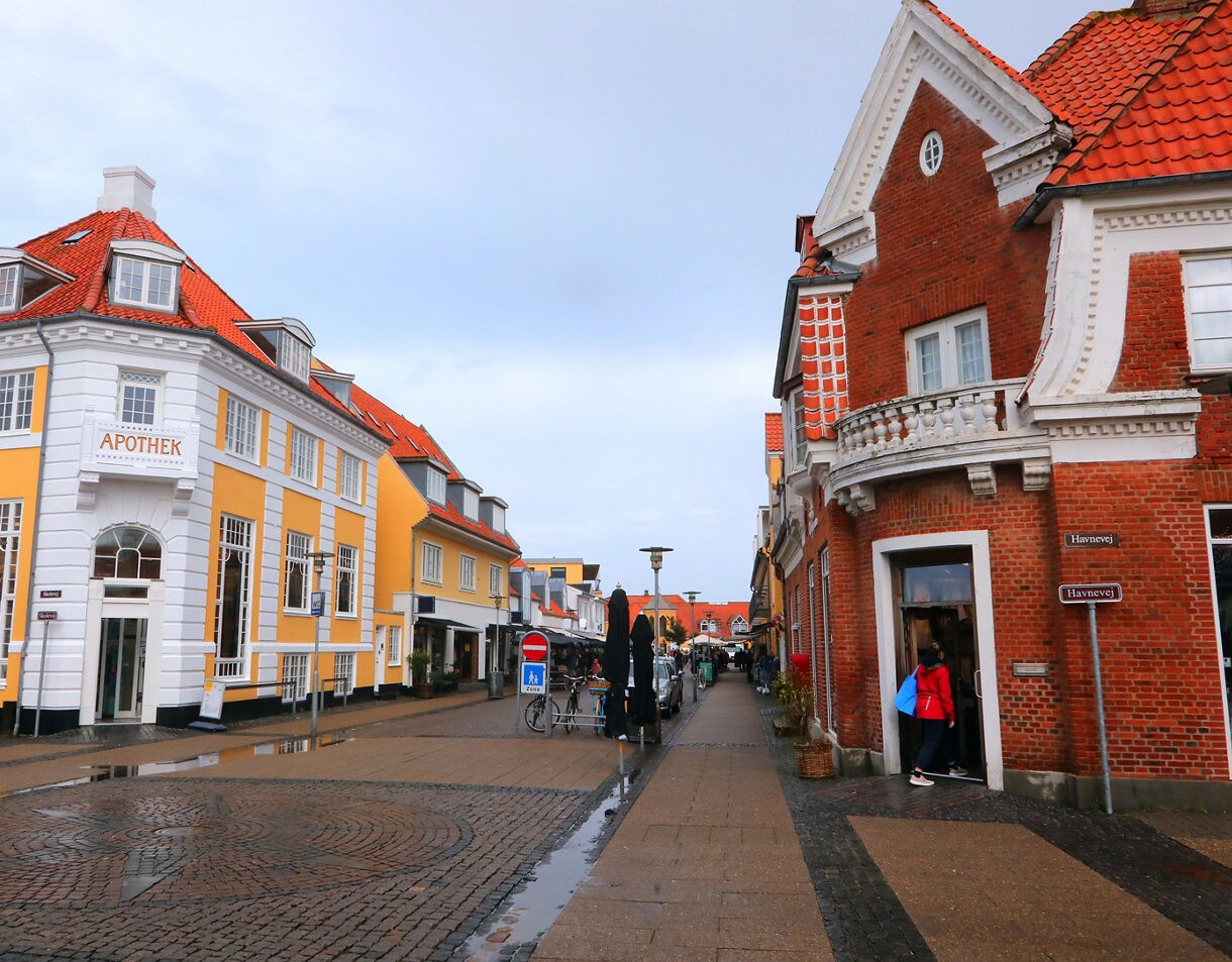 Street view of Skagen with yellow and red brick buildings, cobblestone paths and boutique shops.