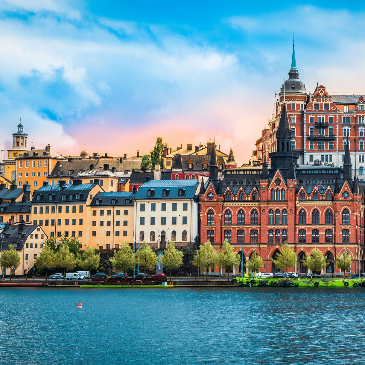 Colorful hillside buildings in Stockholm’s Södermalm district, with ornate red-brick architecture and pastel houses overlooking the water under a vibrant evening sky.