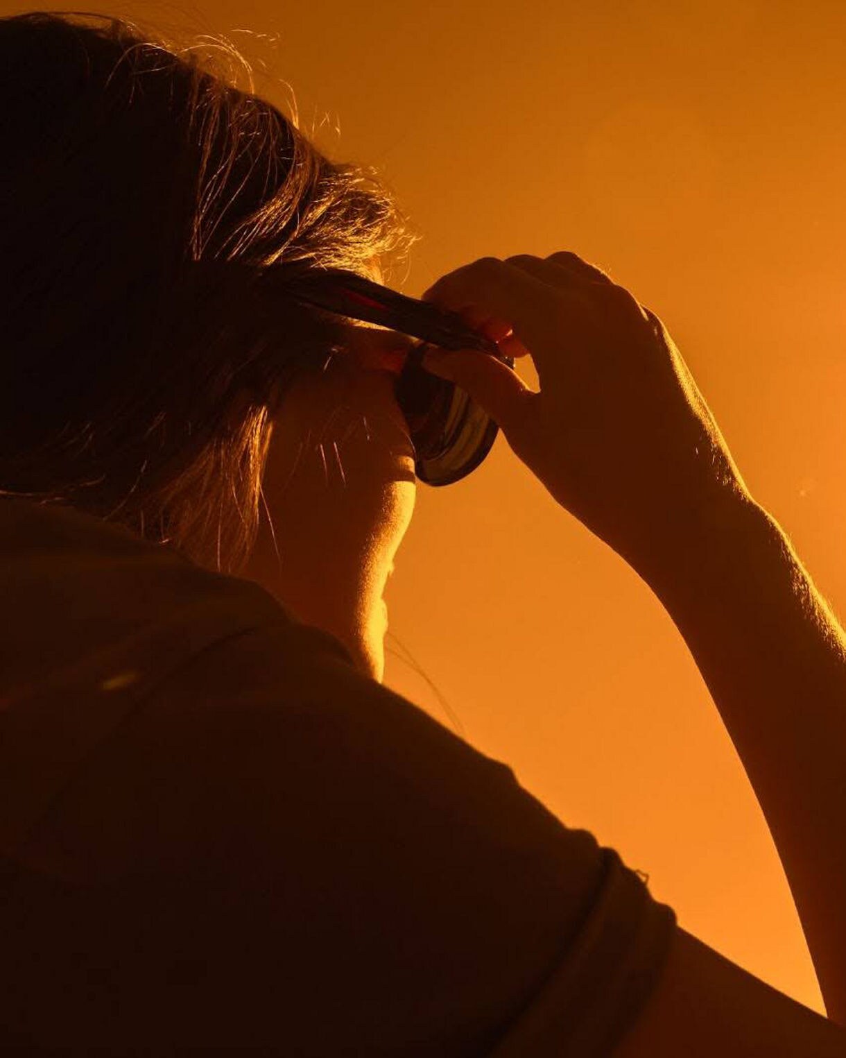 Silhouette of a person lifting eclipse glasses while watching the sun darken against an orange sky.