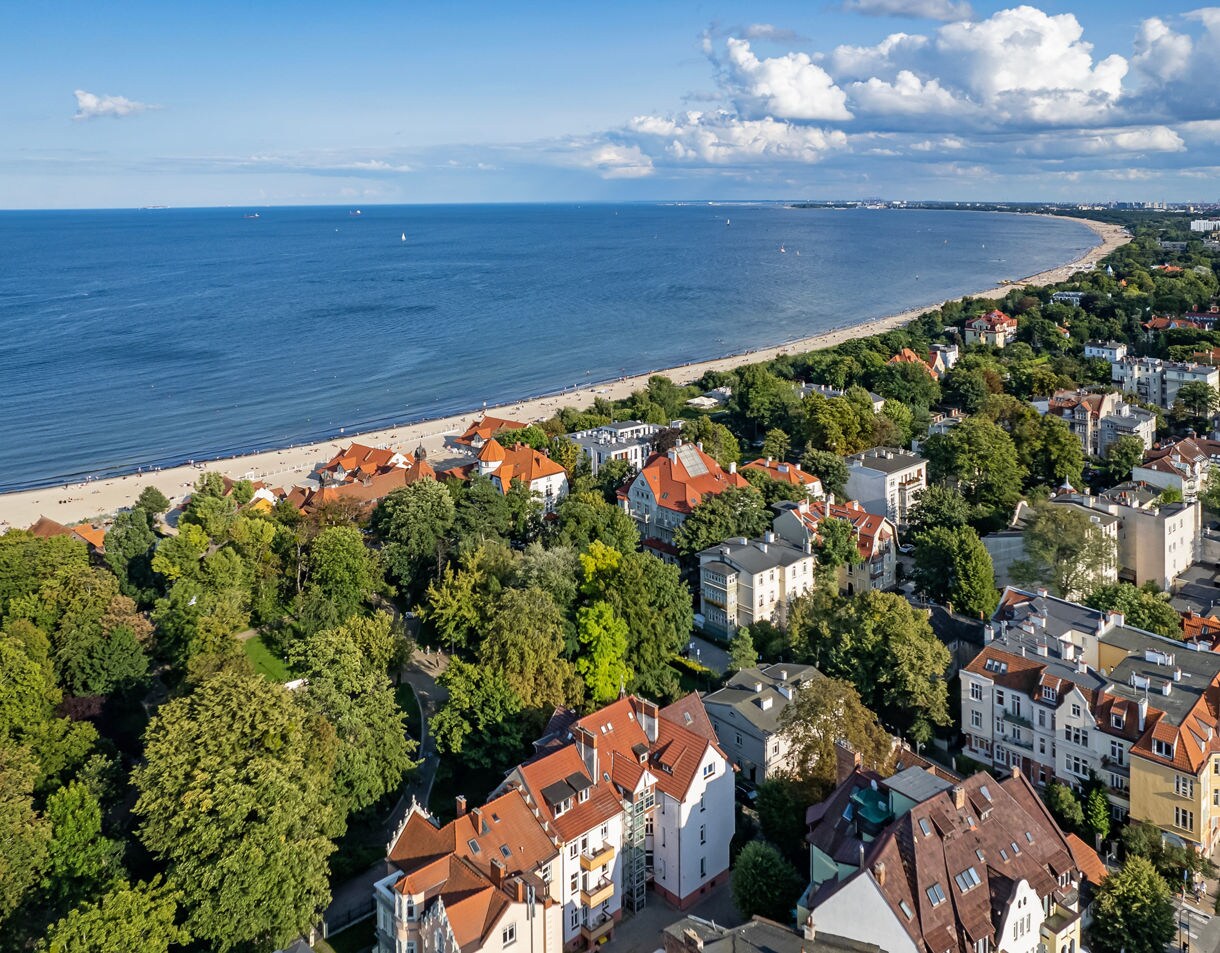 Aerial view of Sopot, Poland, with red-roofed houses, tree-lined streets and a long sandy beach stretching along the Baltic coast.