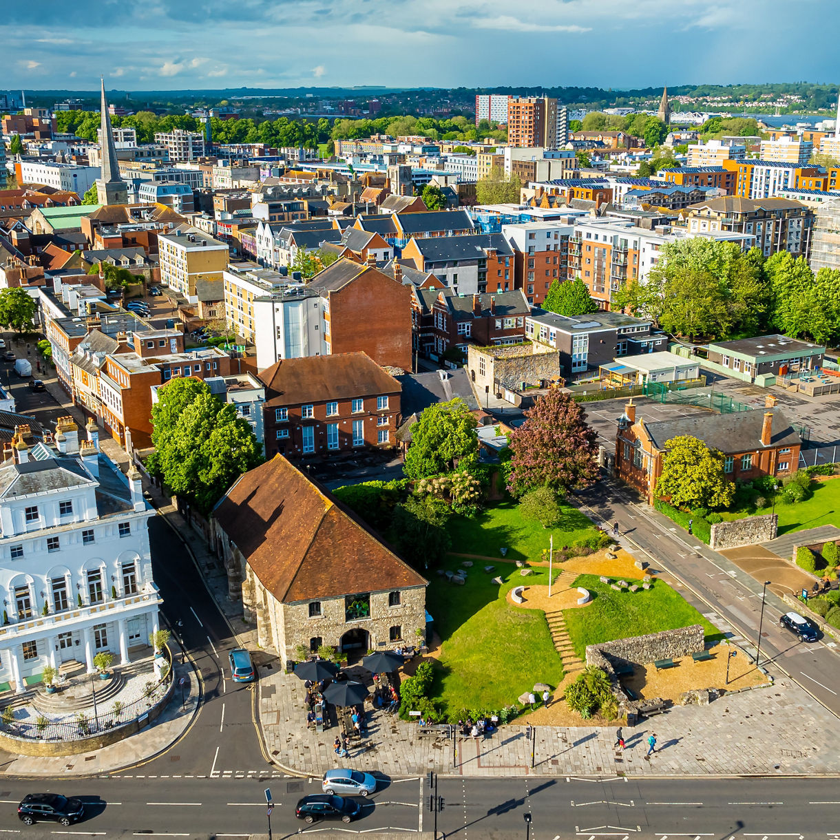 Aerial view of Southampton, England showing a mix of historic and modern buildings, a green park with old stone walls, and a busy street below.