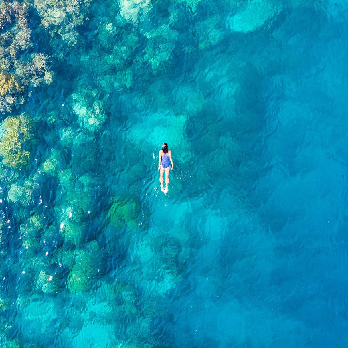 Aerial view of a snorkeler in clear blue water near a colorful coral reef at Cane Bay Beach in St. Croix, surrounded by shades of turquoise and deep blue.
