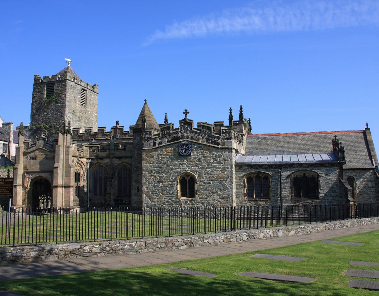 Medieval stone church with a square tower, arched windows and a grassy courtyard under a clear blue sky.