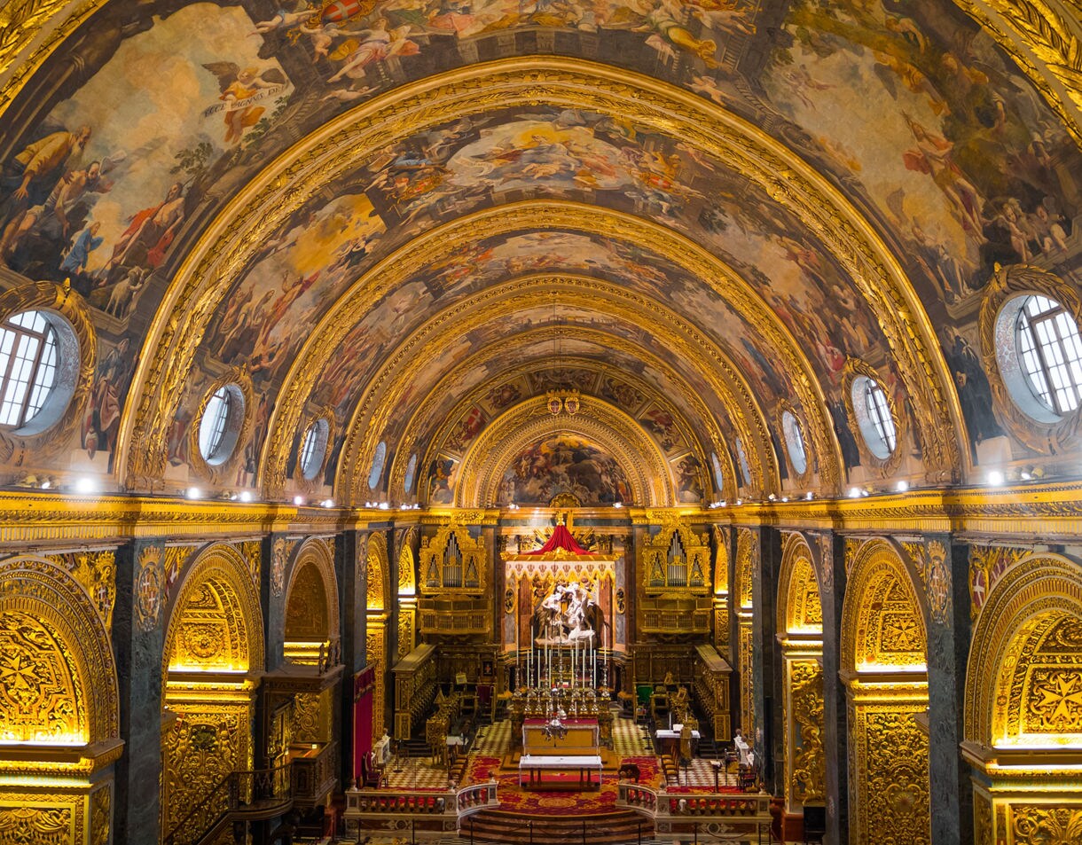 Ornate nave of St. John’s Co-Cathedral in Valletta, Malta, featuring gilded arches, frescoed vaulted ceilings and a richly decorated altar.