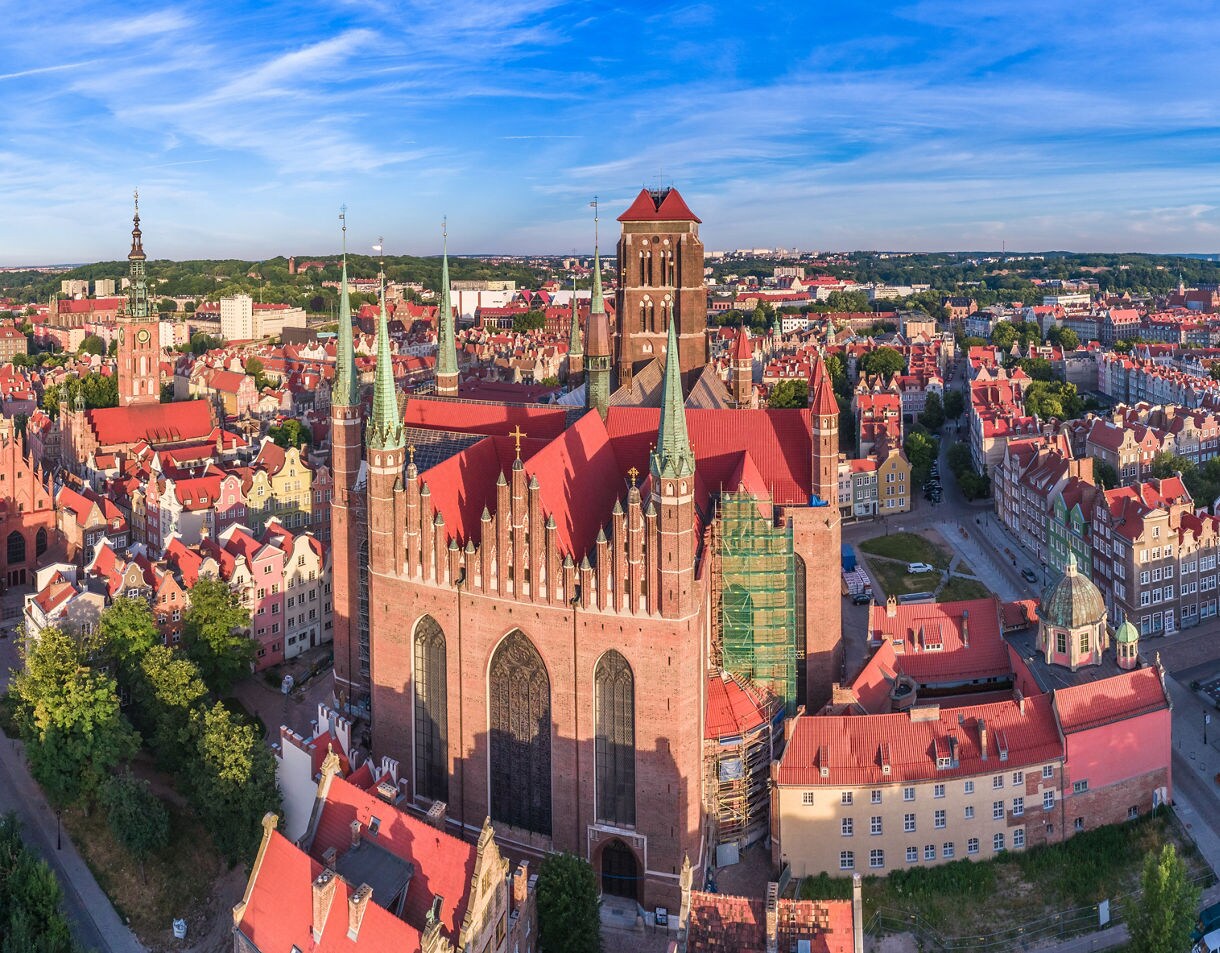 View of Gdańsk’s Old Town waterfront at sunset, with historic red-brick buildings, colorful townhouses, boats on the Motława River and the medieval Crane Gate in the distance.