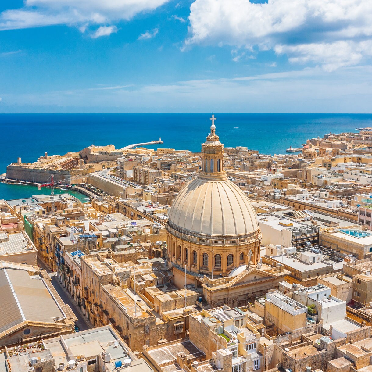 Aerial view of Valletta, Malta, with the prominent dome of St Paul’s Cathedral overlooking the sea and historic limestone buildings.