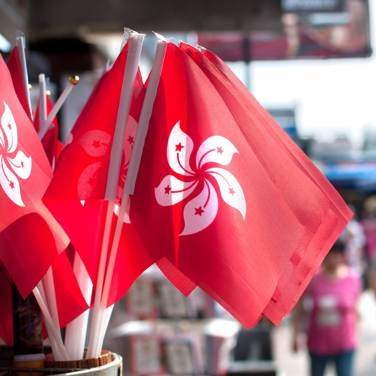 Close-up of Hong Kong flags fluttering at a street market, with blurred crowds shopping in the background.