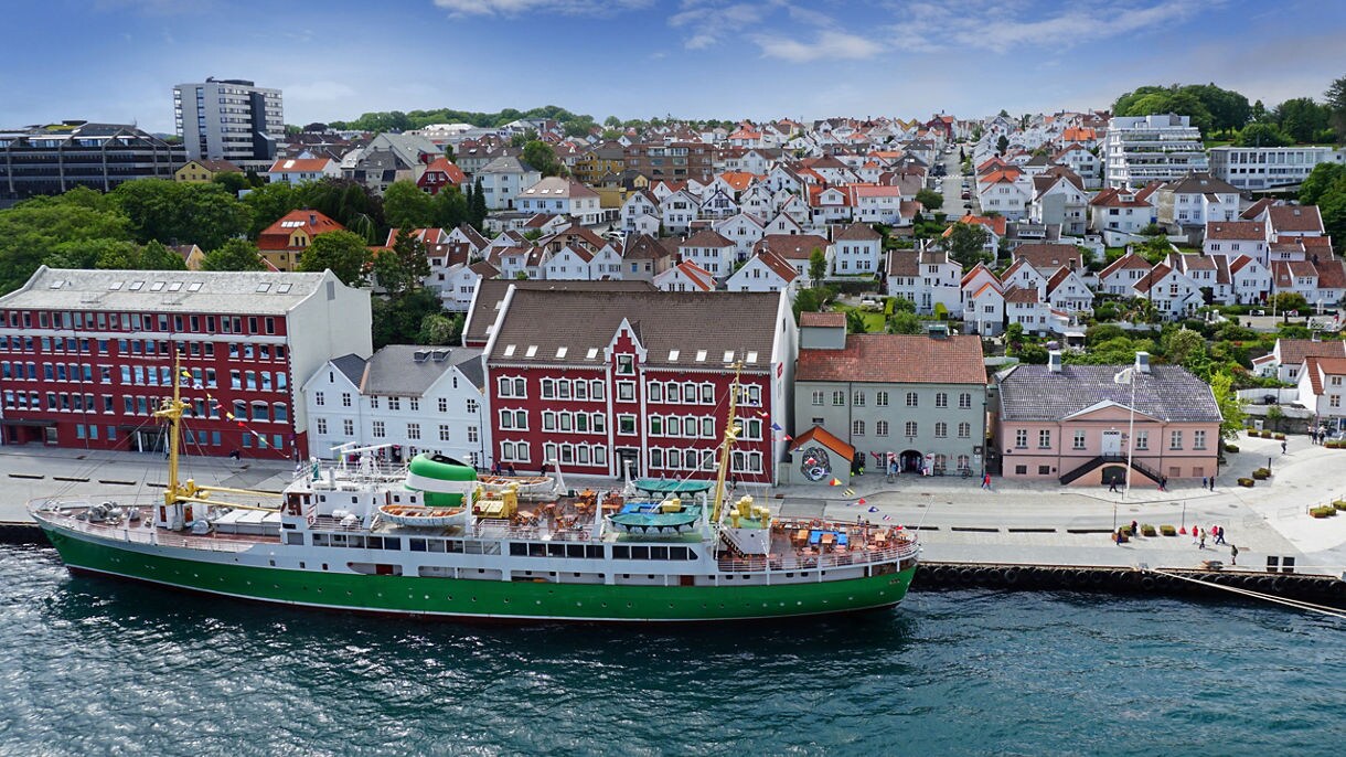 Waterfront view of Stavanger with a docked green and white ship, colorful historic buildings and hillside houses.