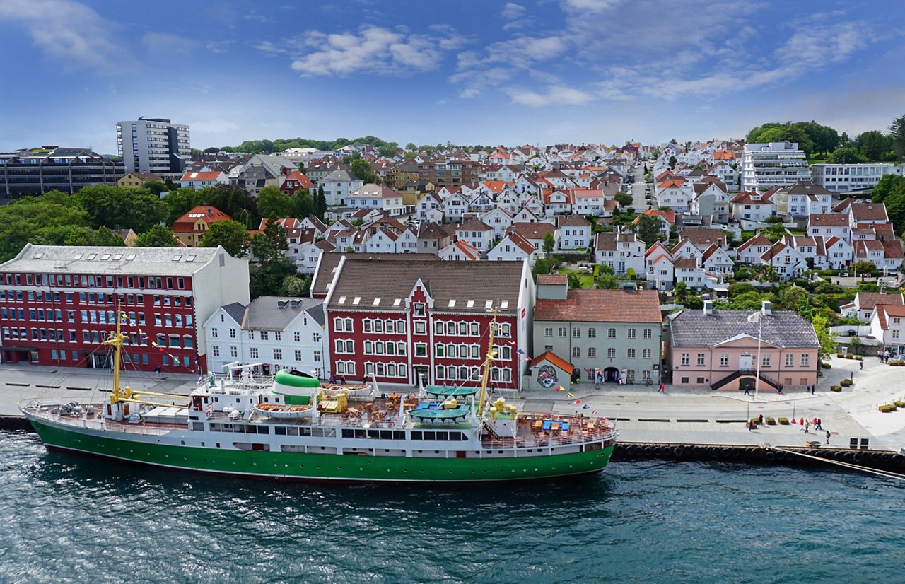 Waterfront view of Stavanger with a docked green and white ship, colorful historic buildings and hillside houses.