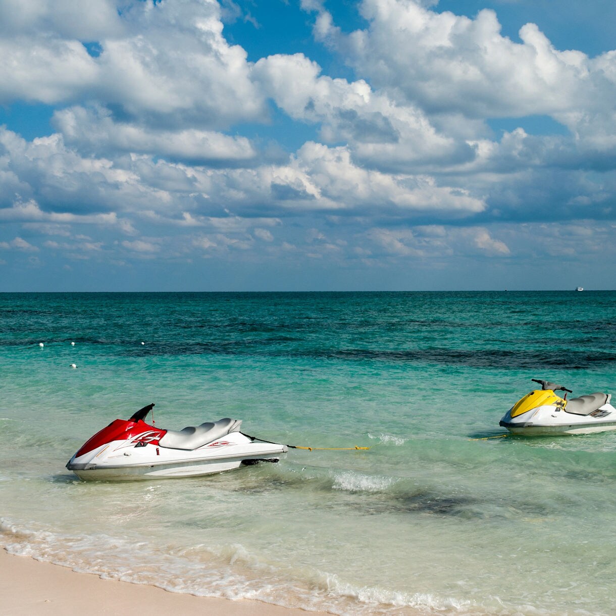 Jet skis floating in shallow turquoise water near the sandy shore of Taino Beach in the Bahamas.