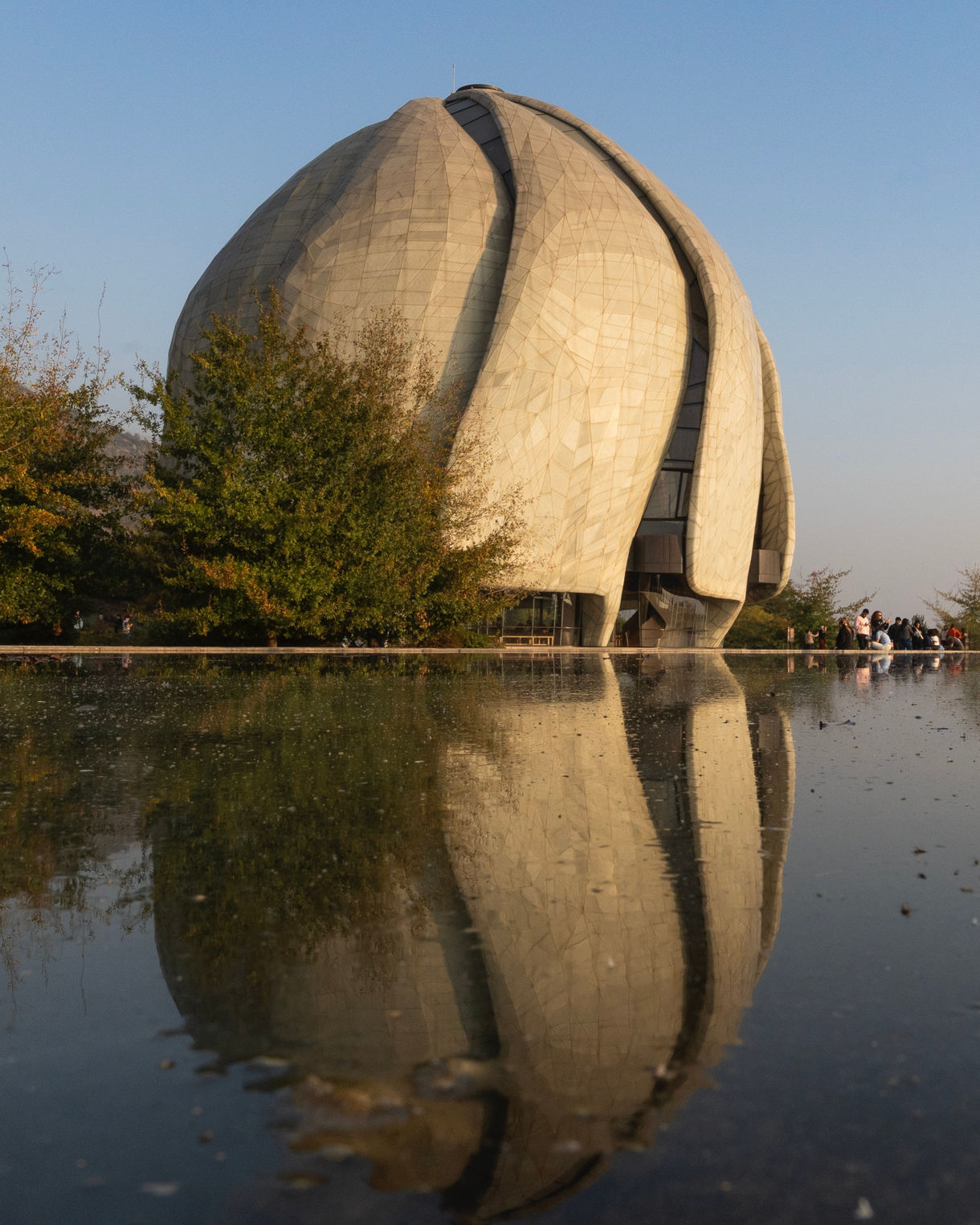 The Bahá’í Temple in Santiago with its curved, petal-like facade lit by warm sunlight, reflected clearly in a calm pool in the foreground.