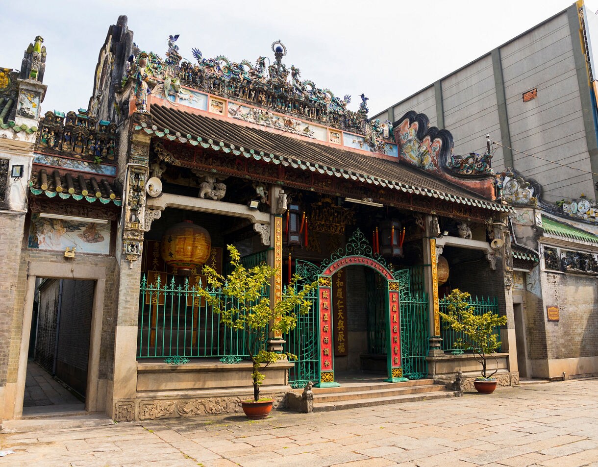 Exterior of Thien Hau Pagoda with detailed roof carvings, teal gates, hanging lanterns and weathered stone walls in Ho Chi Minh City.