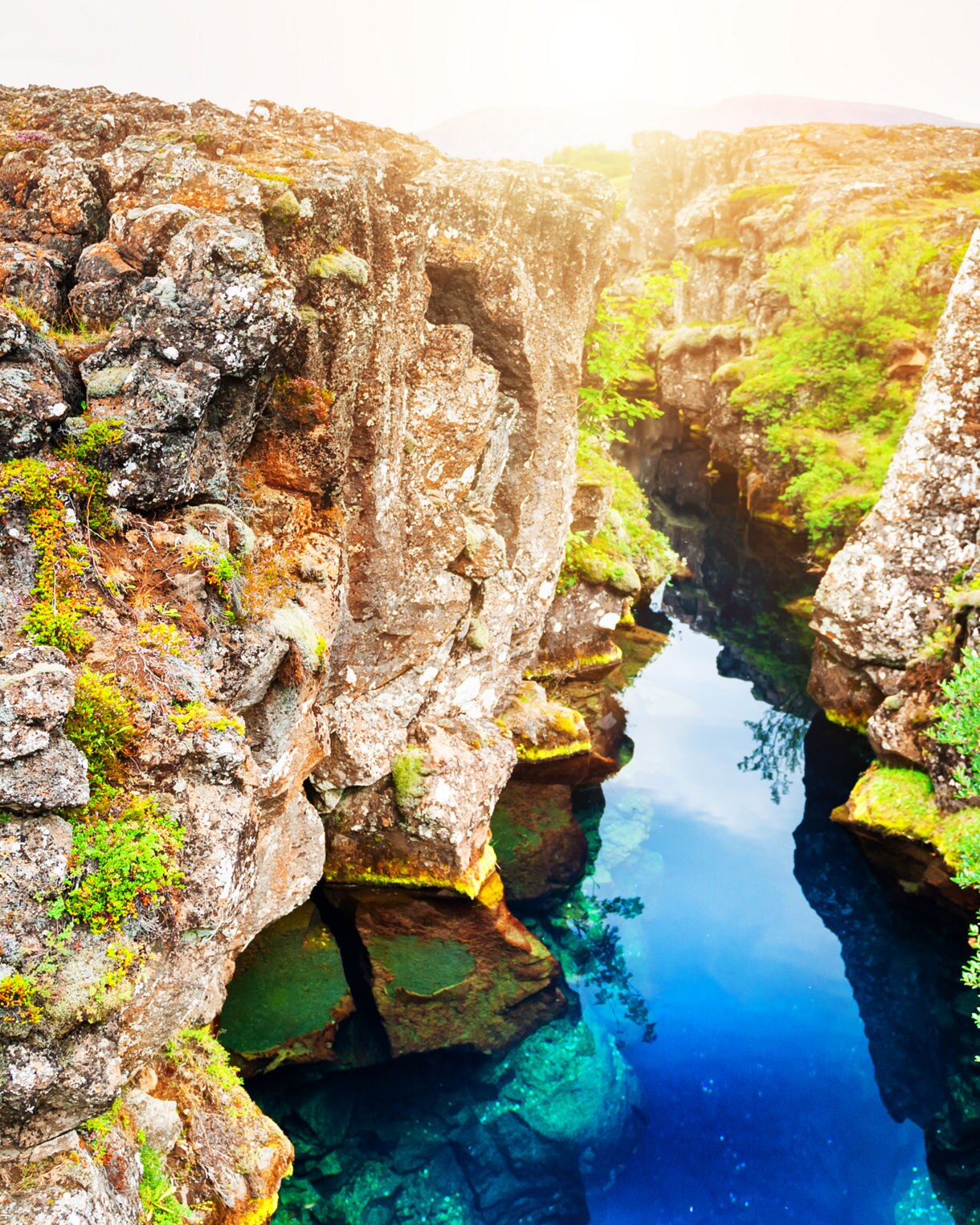 Clear blue water flowing between rocky cliffs covered in moss and greenery at Thingvellir National Park in Iceland.