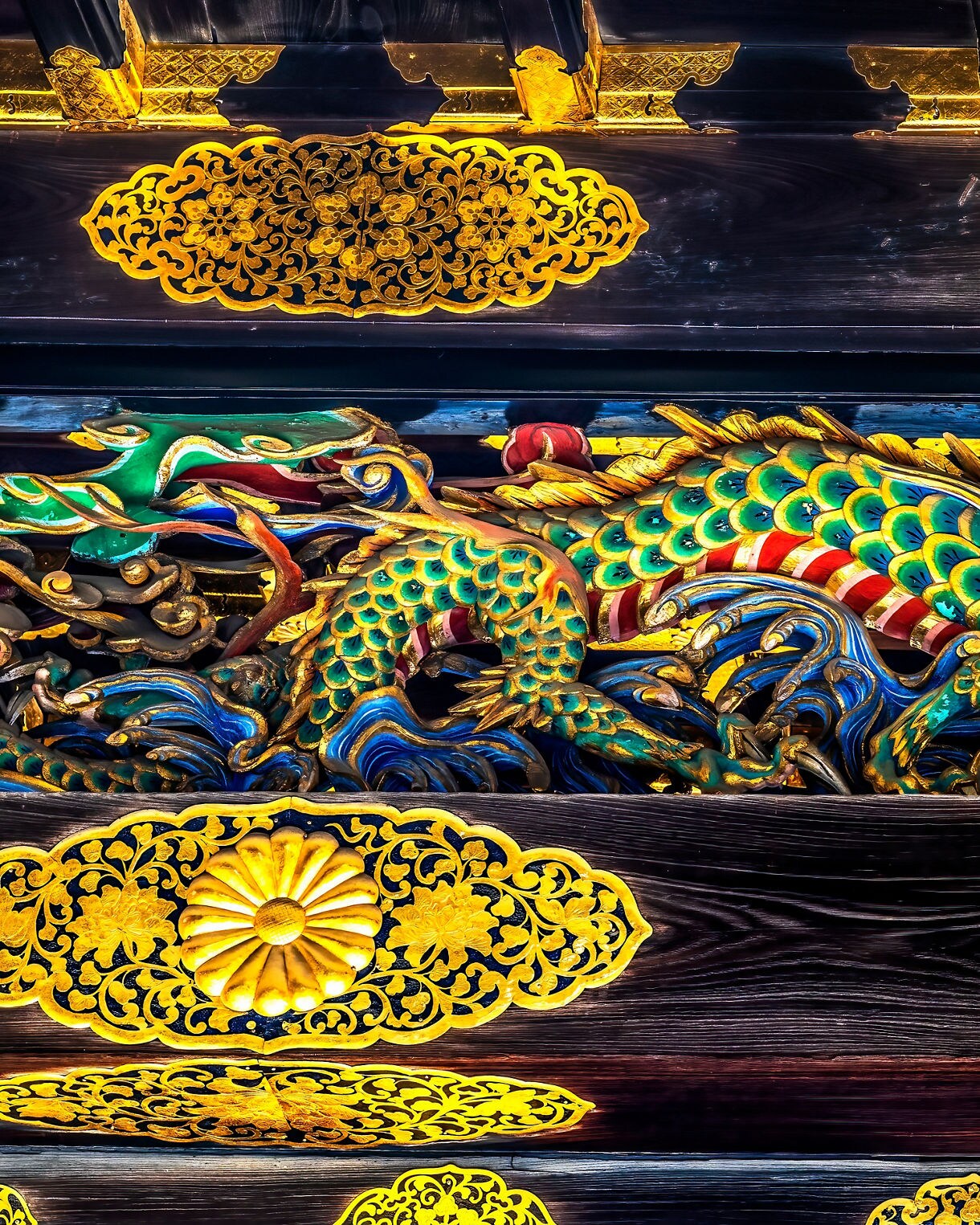 Intricate wooden carving of a multicolored dragon surrounded by vivid gold embellishments, set against dark lacquered beams and ornate gilded floral motifs.