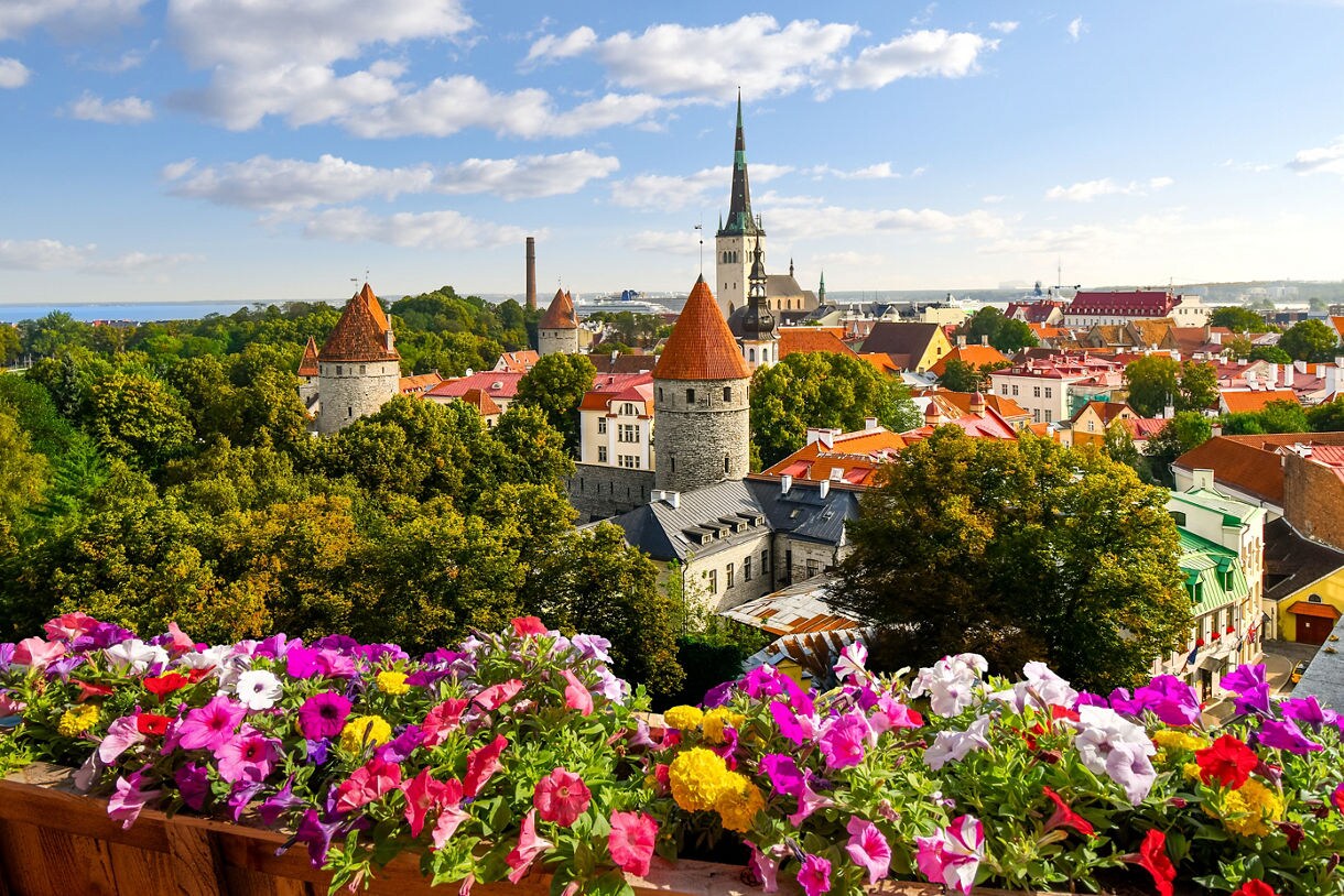 View of Tallinn, Estonia, from Toompea Hill with stone towers, church spires and red-tiled rooftops framed by bright flower boxes in the foreground.