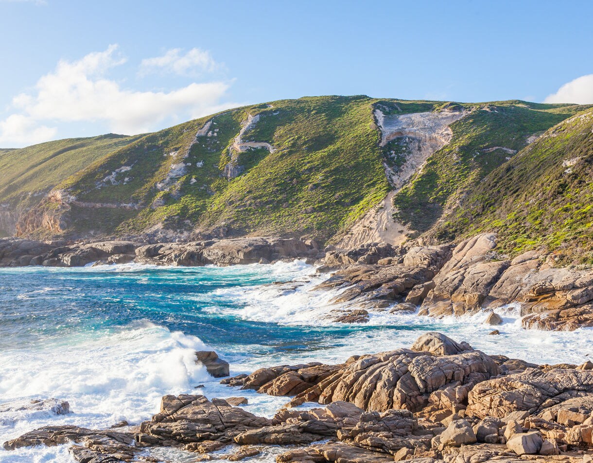Rocky shoreline with turquoise waves hitting steep green cliffs.