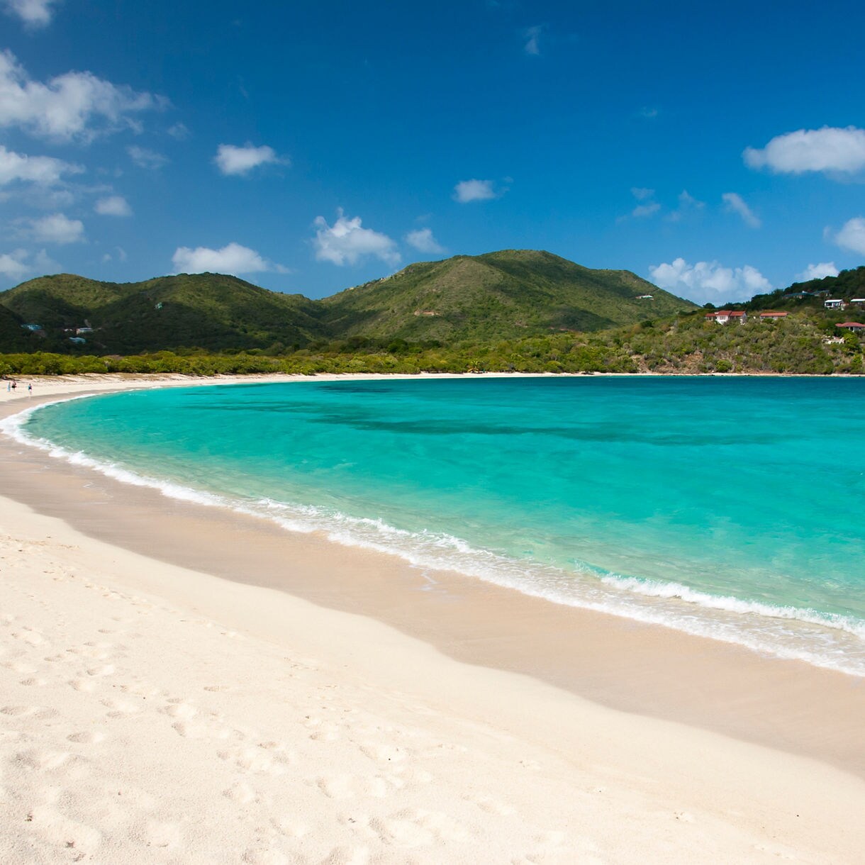 Turquoise water curves along a white sand beach, backed by green hills and a scattering of hillside villas.