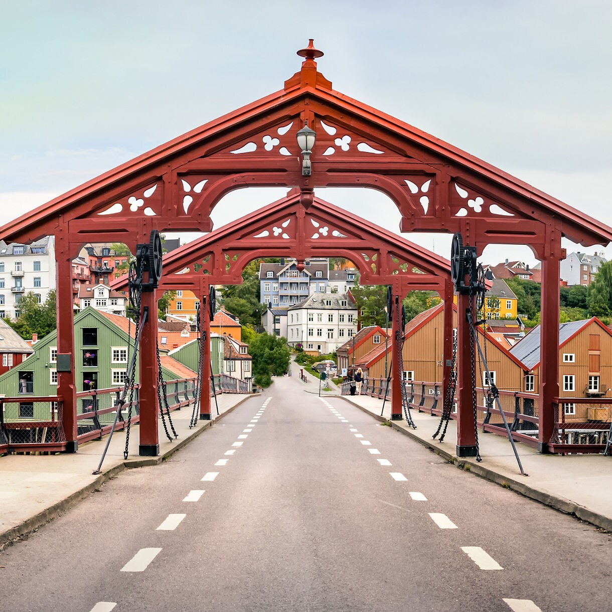 Historic red wooden Old Town Bridge in Trondheim leading to rows of colorful wooden wharf buildings along the Nidelva River.