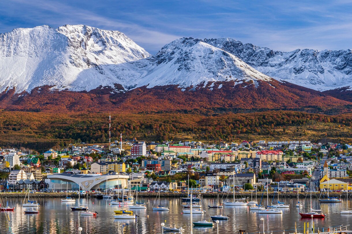 Colorful buildings and a marina full of boats in Ushuaia with towering snow-covered mountains in the background.