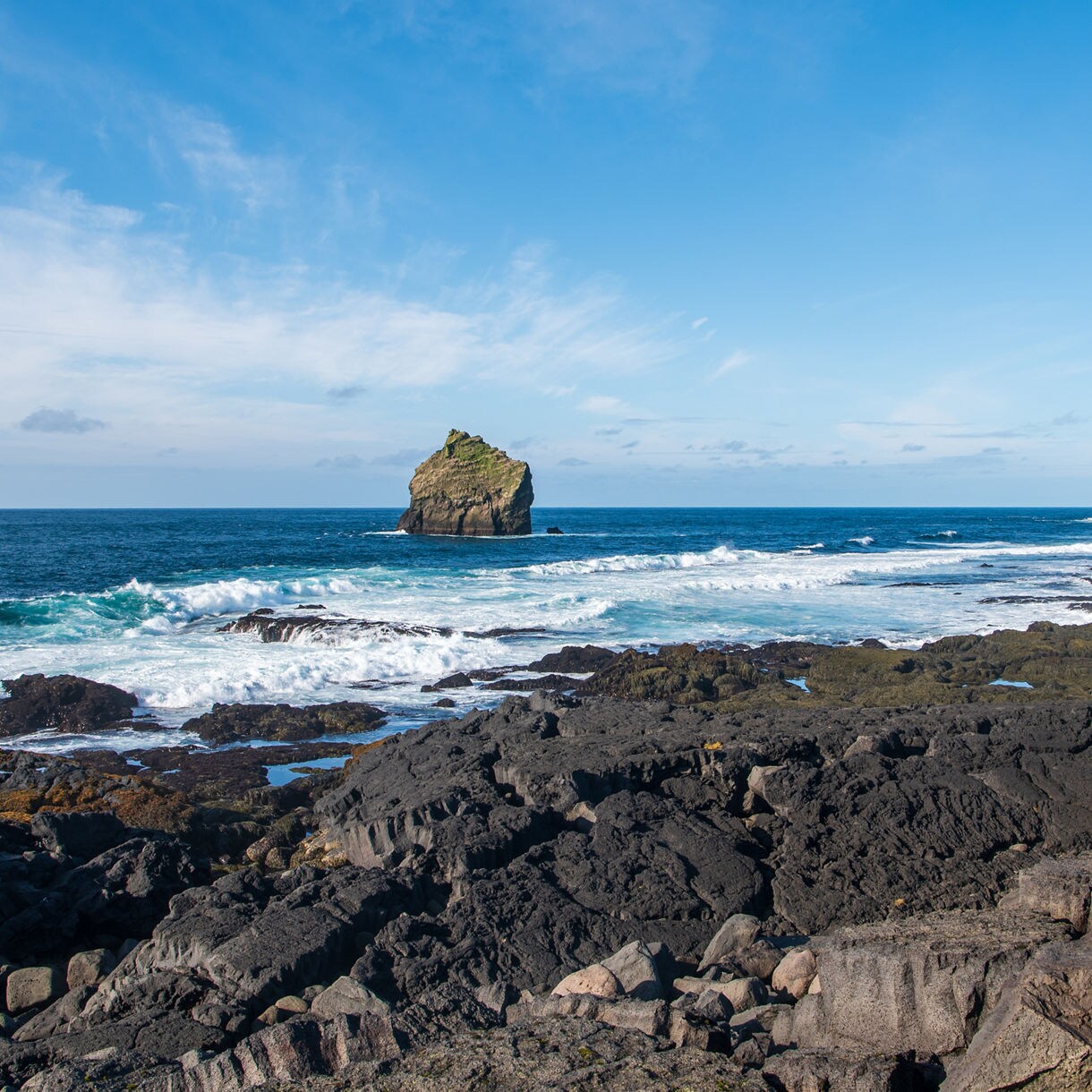 Valahnúkamöl cliffs on Iceland’s Reykjanes Peninsula, showing black volcanic rock shoreline with waves breaking and a solitary sea stack rising from the Atlantic Ocean.
