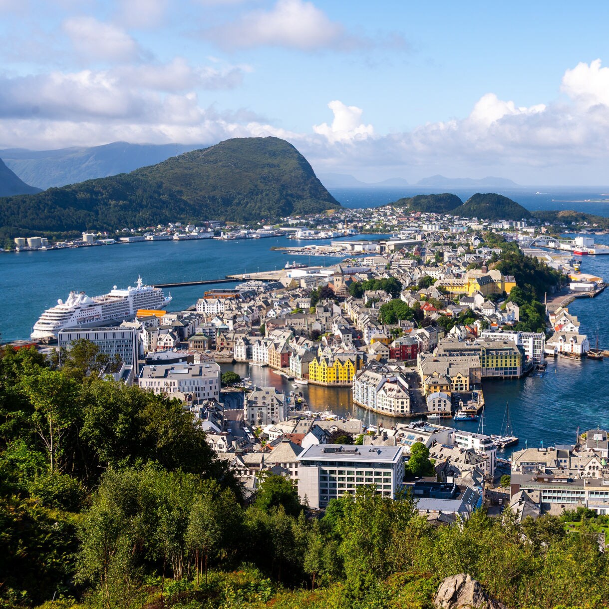 Elevated view of Ålesund’s town center with colorful buildings, a cruise ship docked at the harbor and mountains in the distance.
