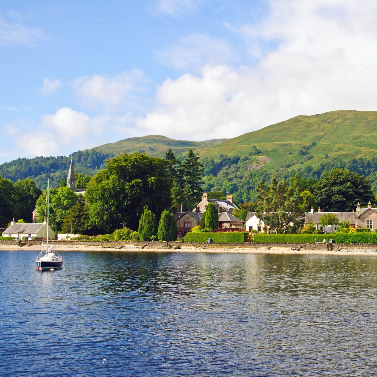 Small village of Luss on Loch Lomond, with stone cottages, lush greenery and hills rising in the background.