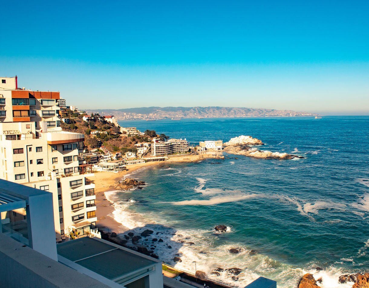 Coastal view of Viña del Mar with sandy coves, rocky shoreline and tall beachfront buildings overlooking deep blue Pacific water.