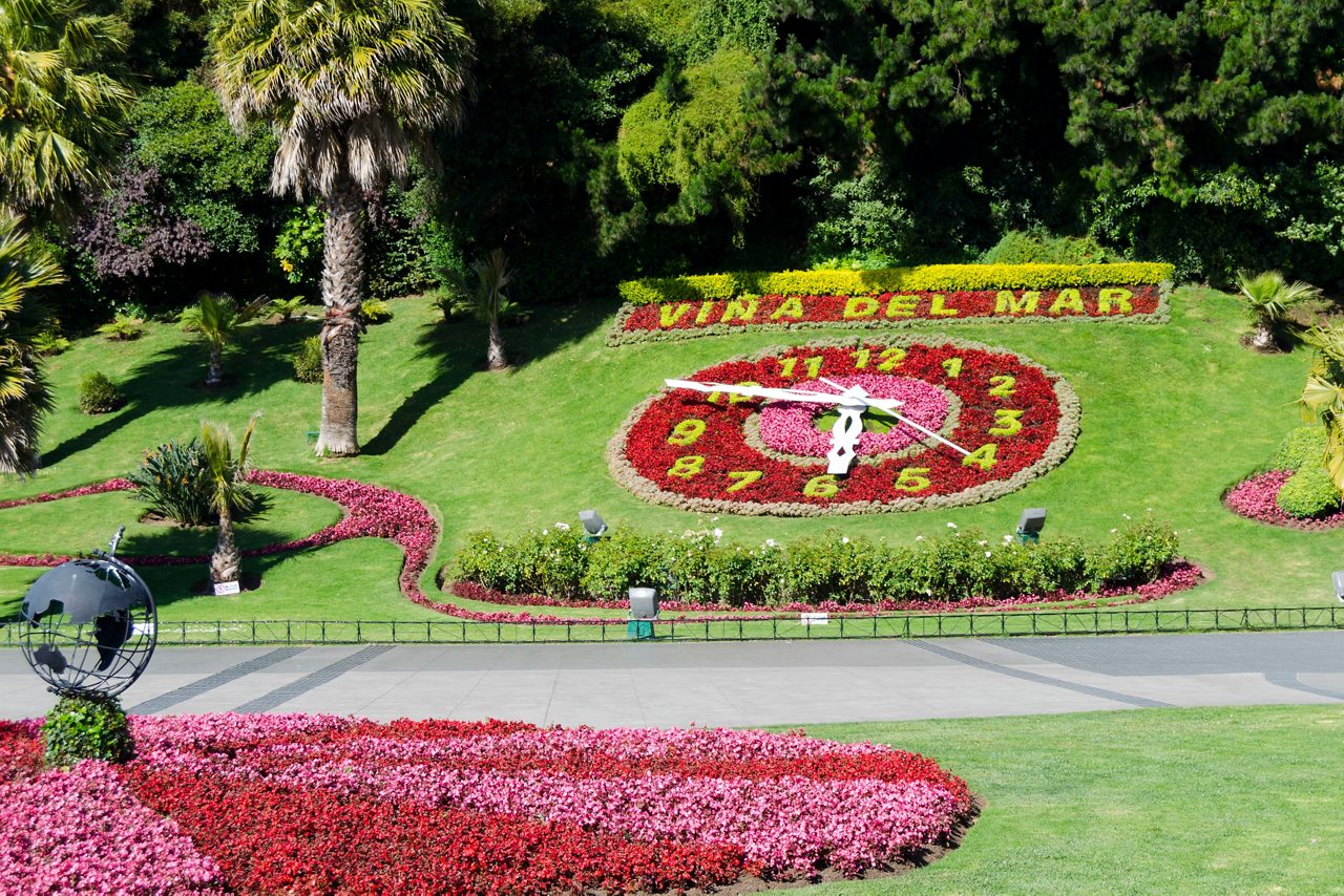 Large floral clock in Viña del Mar made of bright red, yellow and pink flowers set into a green hillside.