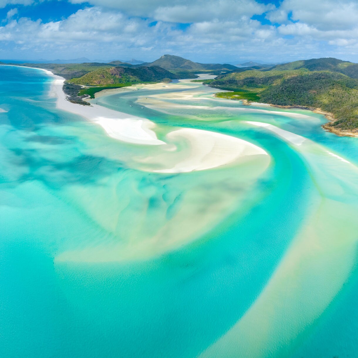Aerial view of Whitehaven Beach showing turquoise water blending with white silica sand and lush green hills.
