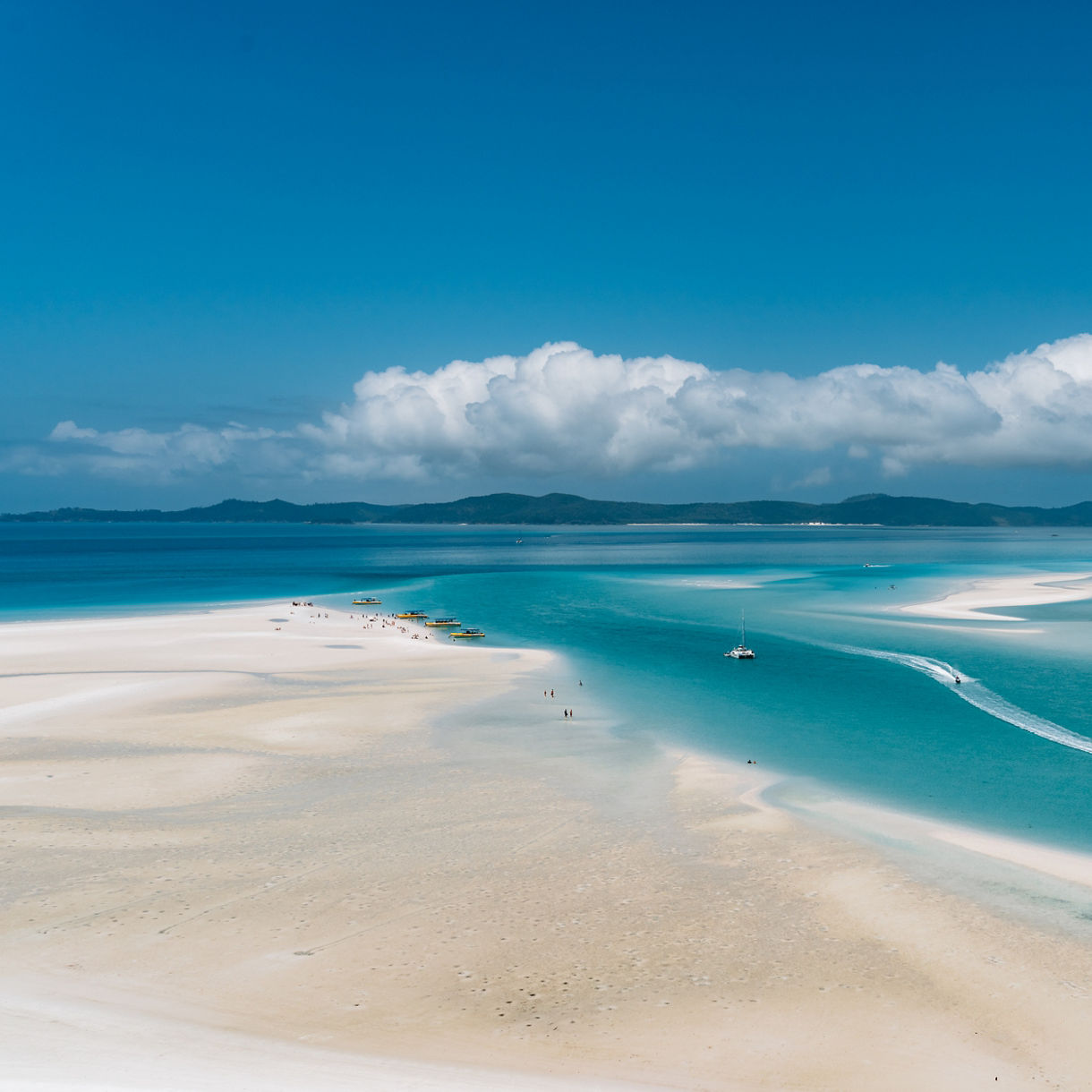Aerial view of a boat gliding through the vivid turquoise waters and white sandbars of Whitehaven Beach lagoon.