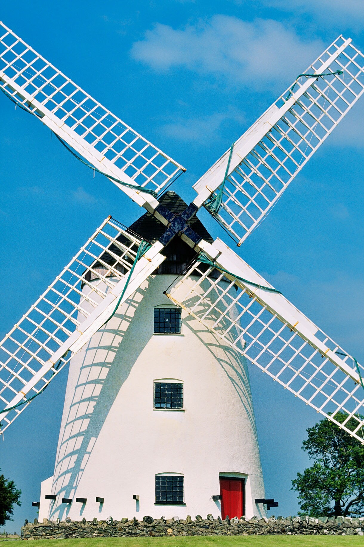 White windmill with large lattice blades and a red door set against a clear blue sky.