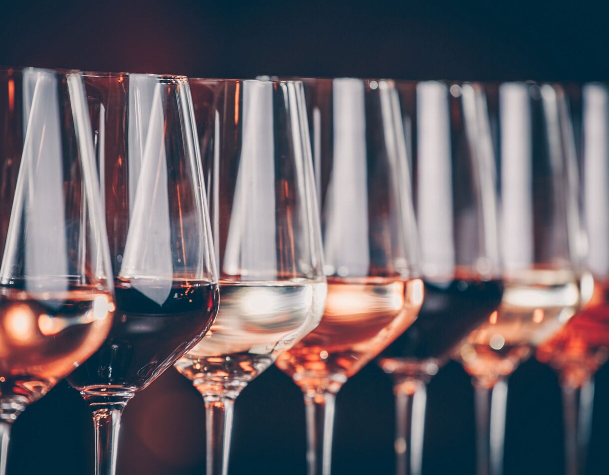 A row of wine glasses filled with different shades of wine, from pale to deep red.
