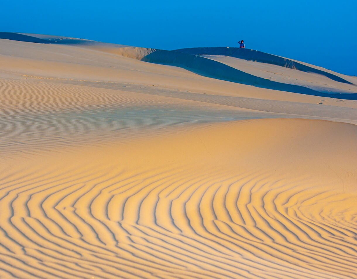 Soft golden light over smooth sand dunes at sunset with gentle ripples in the foreground.