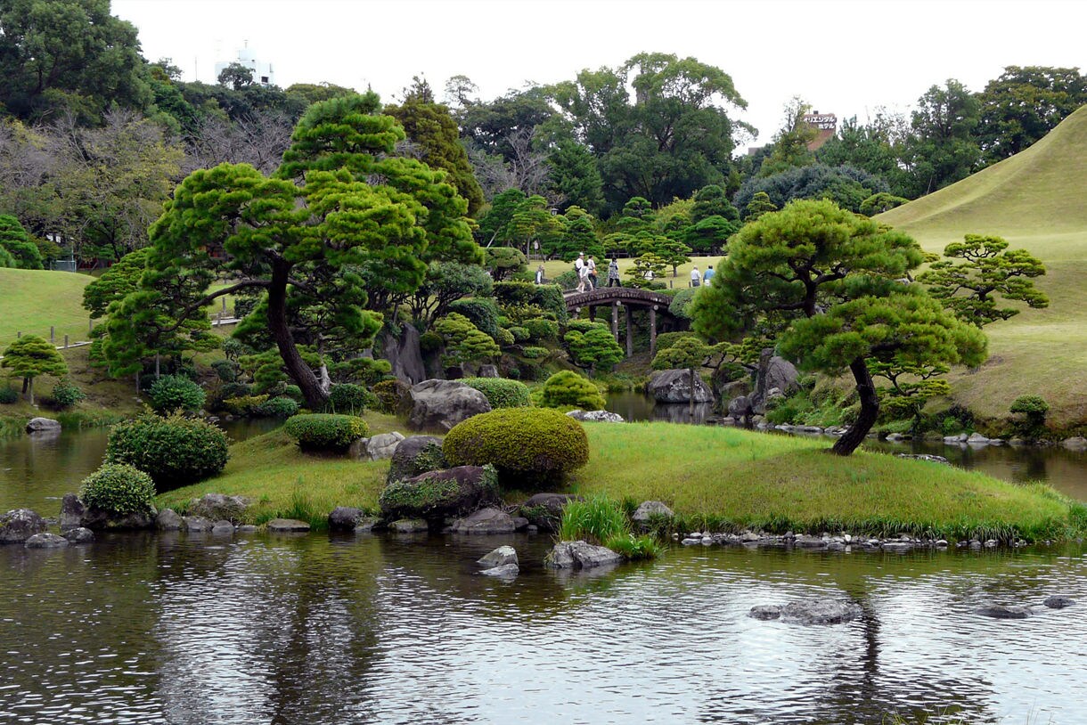 A traditional Japanese garden featuring manicured trees, a pond, and a smooth conical hill.